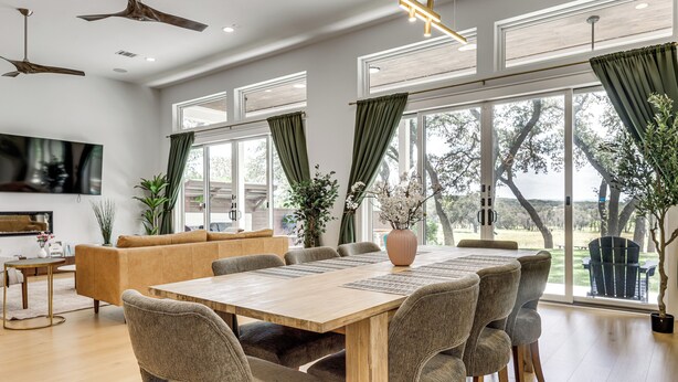 A spacious dining area with a wooden table and chairs, a sofa, and large windows with curtains. - Pool & Lake Access! Dual Homes on Canyon Lake (Canyon Lake)