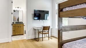A bedroom with a bunk bed, a desk with a chair, a television, and a bathroom with a mirror and sink. - Pool & Lake Access! Dual Homes on Canyon Lake (Canyon Lake)