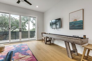 A modern room with a pool table, a flat-screen TV mounted on the wall, and a large window with a view of trees. - Pool & Lake Access! Dual Homes on Canyon Lake (Canyon Lake)