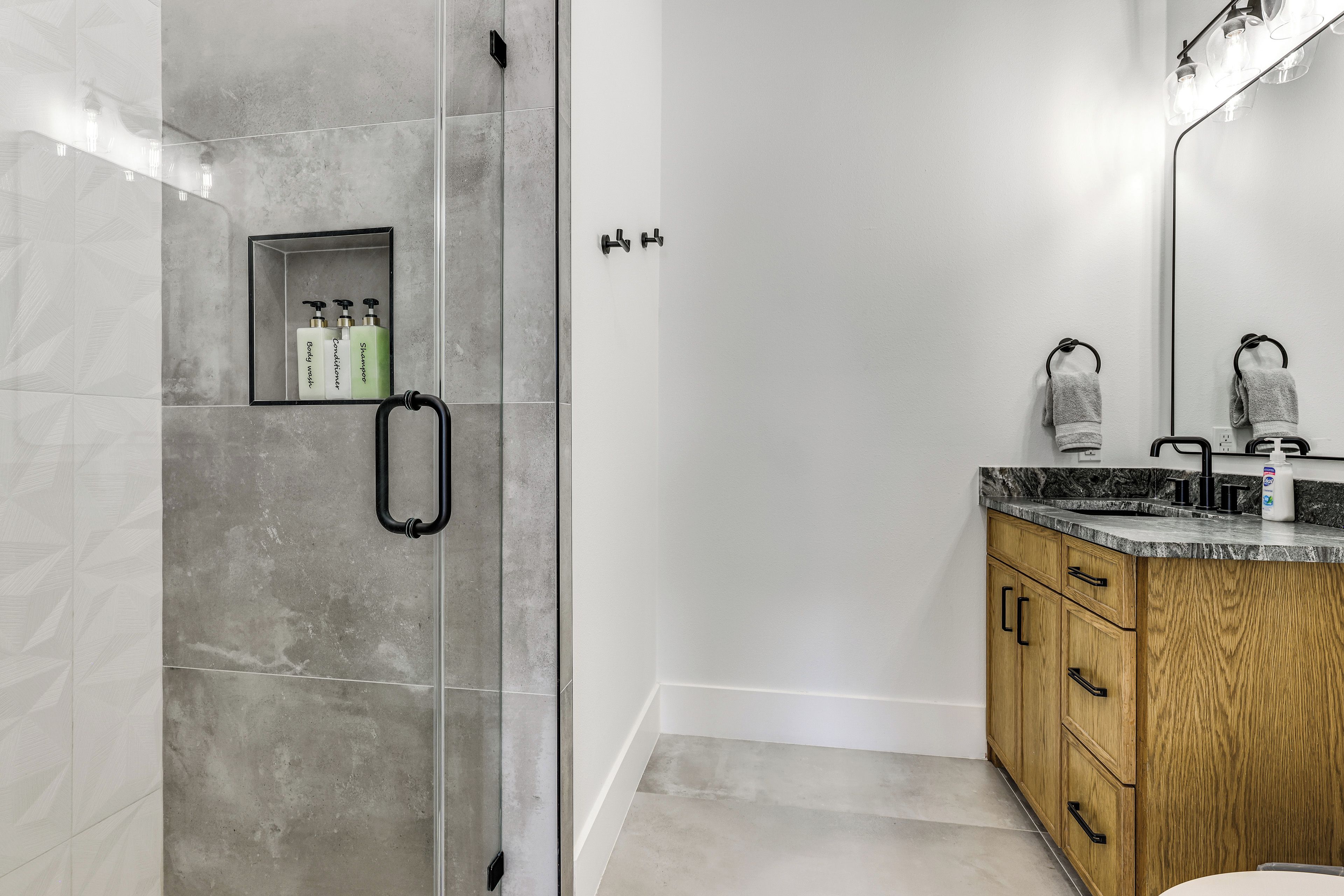 A modern bathroom with a glass shower enclosure, a wooden vanity with a marble countertop, and a large mirror above the sink.
