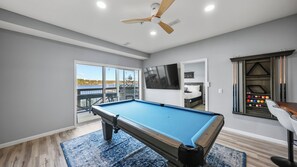 A pool table in a room with a ceiling fan, a window with a view, and a wall-mounted TV. - Waterfront Oasis with Theater, Game Room, 2 King Suites, 2 Pools, Boat Slip (Osage Beach)
