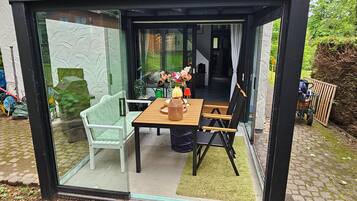 Eine verglaste Terrasse mit Tisch, Stühlen und einem kleinen Garten im Hintergrund.
