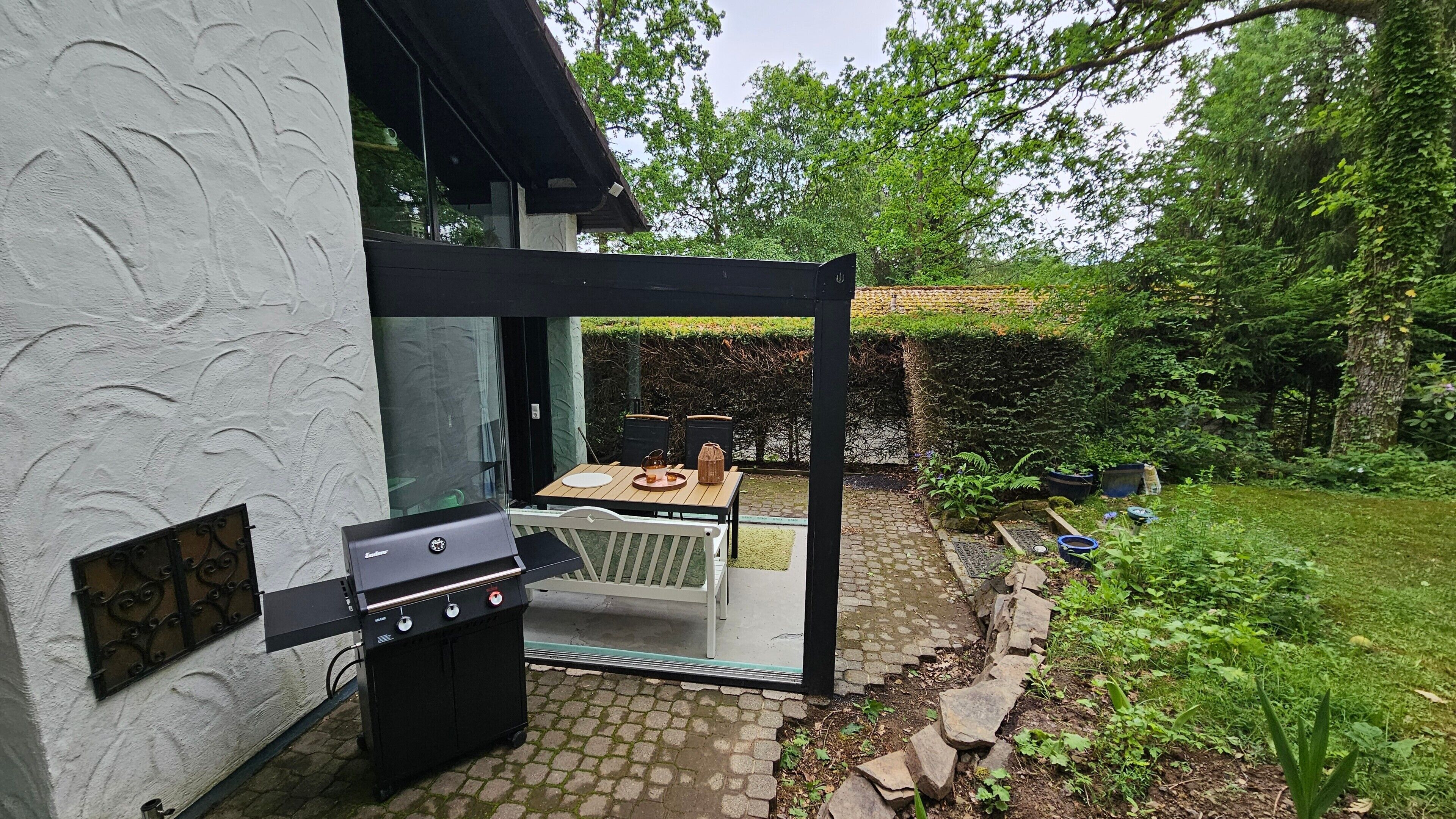 Eine Terrasse im Freien mit Grill, Tisch und Stühlen sowie einer Glasveranda.