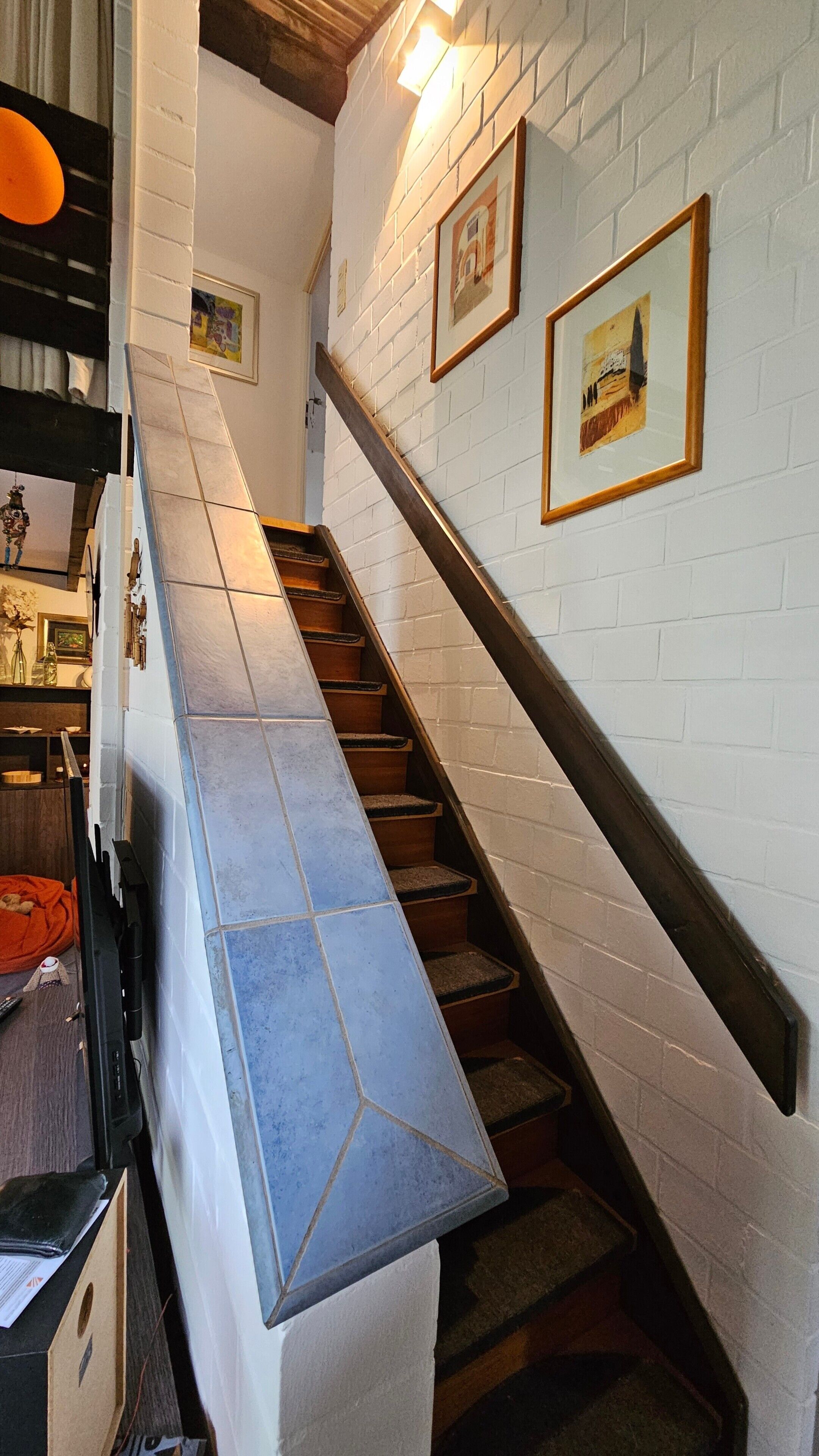 Una escalera con pared de ladrillo blanco y barandal de madera, que conduce a un piso superior.