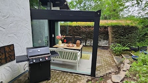 An outdoor patio with a grill, a table with chairs, and a garden area.
