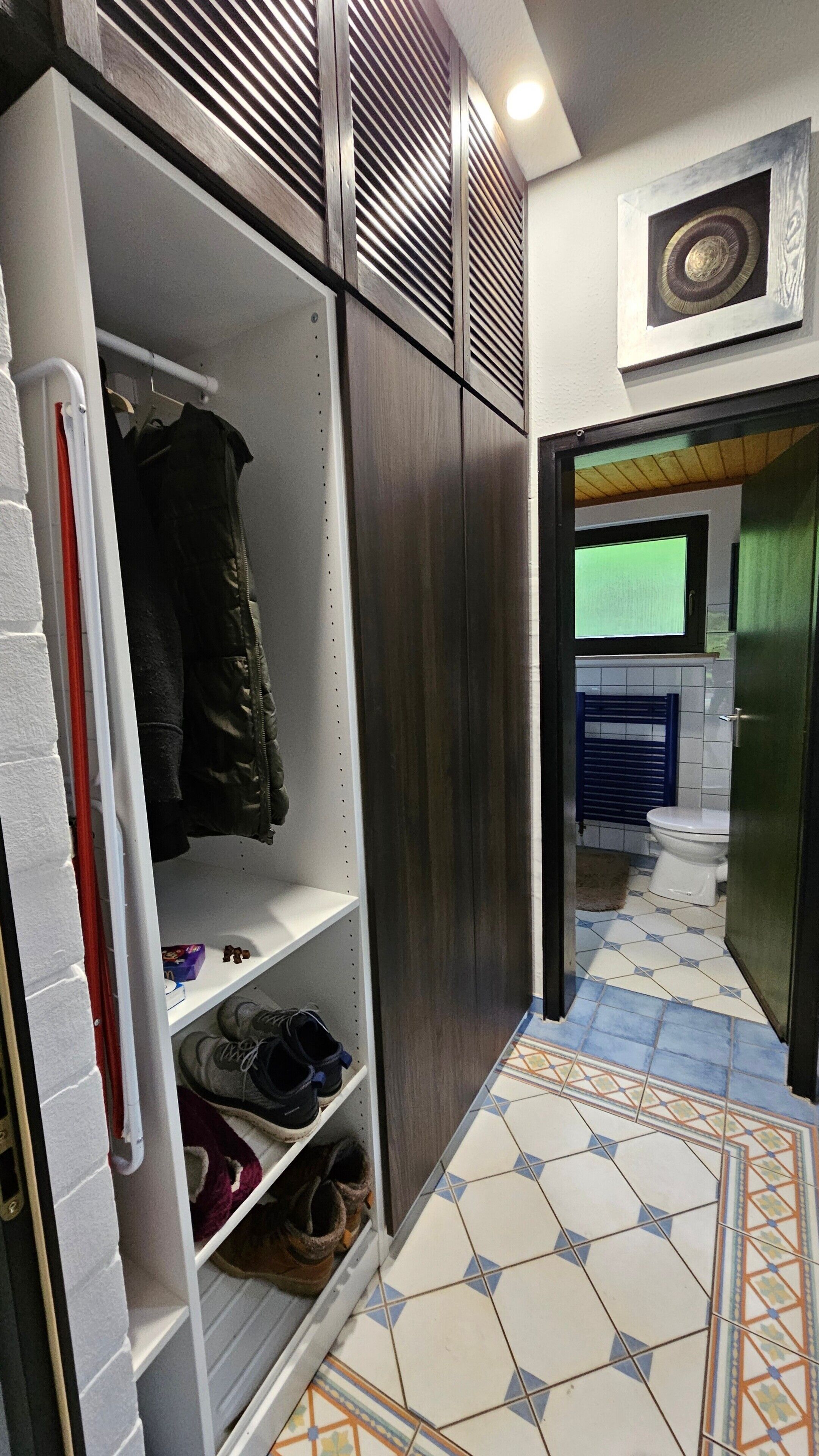 Ein schmaler Flur mit einem Schrank, gefliestem Boden und einem Badezimmer mit Toilette und Dusche.