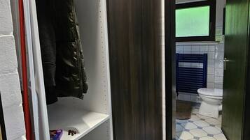Ein schmaler Flur mit einem Schrank, gefliestem Boden und einem Badezimmer mit Toilette und Dusche.