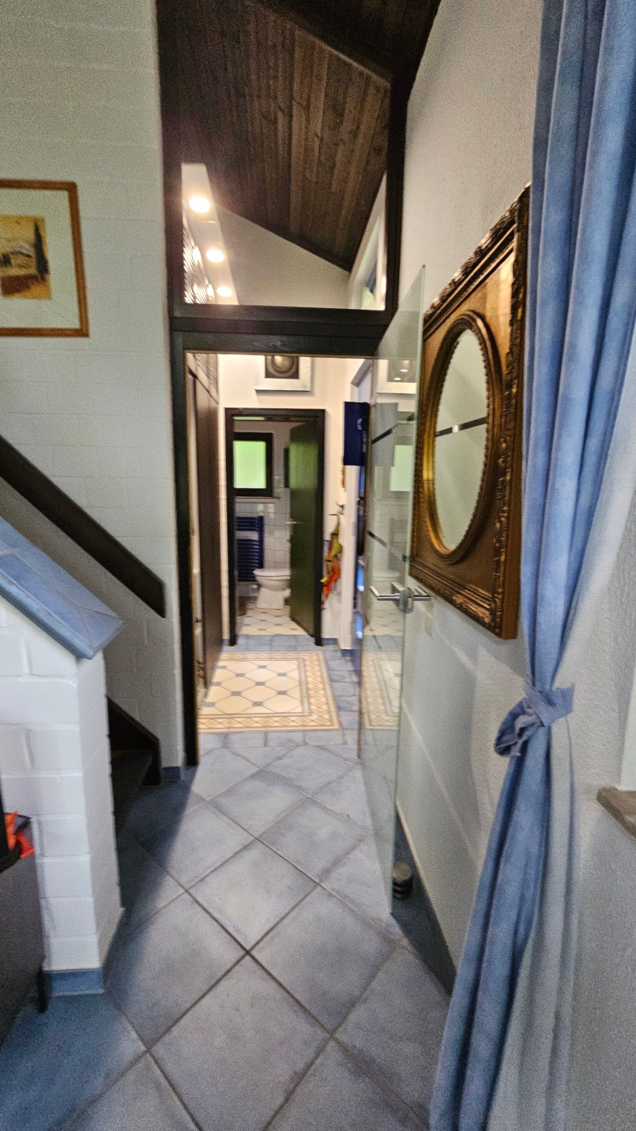 A hallway with a tiled floor, a mirror on the wall, and a staircase on the left.