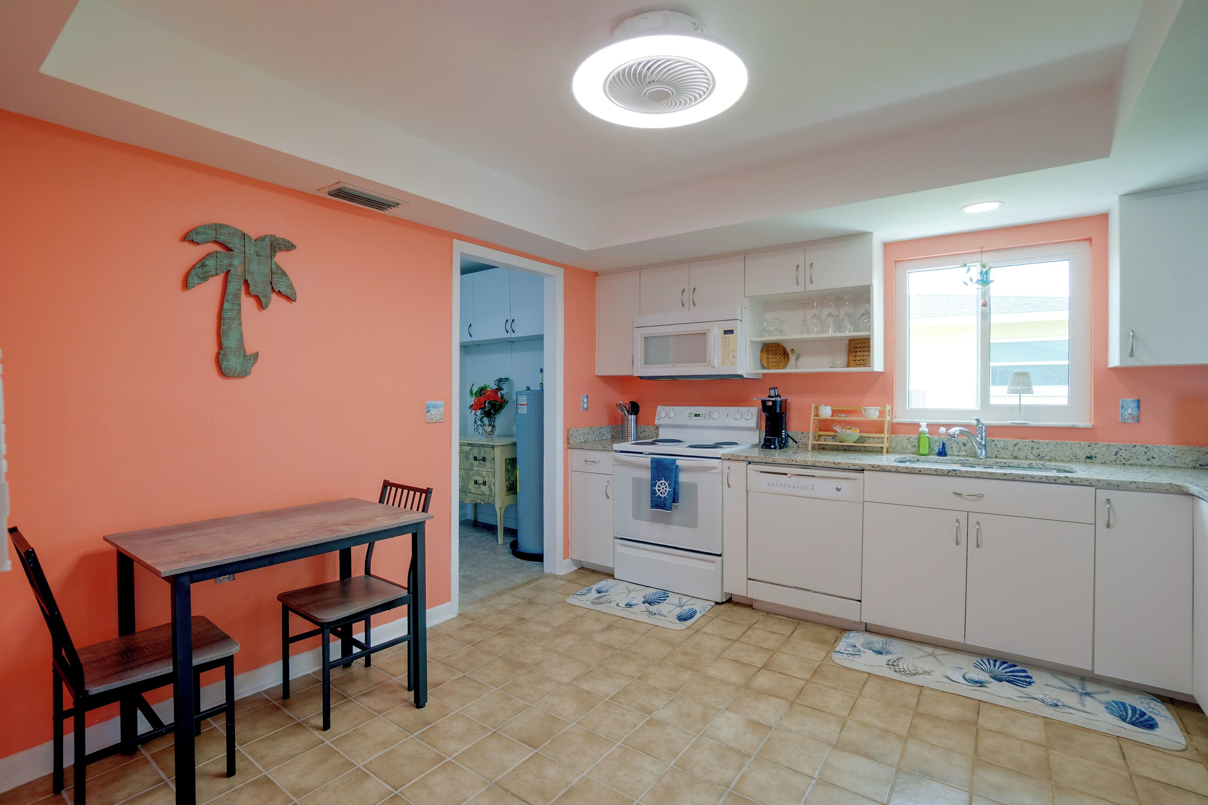 Une cuisine avec des meubles blancs, un four à micro-ondes, une cuisinière et un évier. On y trouve également une table à manger avec des chaises.