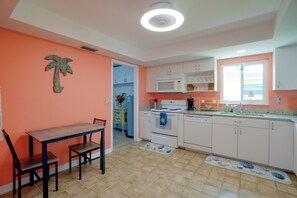 A kitchen with white cabinets, a microwave, a stove, and a sink. There is a dining table with chairs.