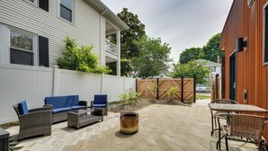 Eine Terrasse mit Gartenmöbeln, einer Feuerstelle und einem weißen Zaun.