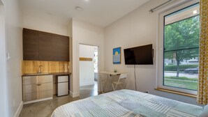 Ein Schlafzimmer mit einem Bett, einem Schreibtisch, einem Fernseher und Blick ins Freie.