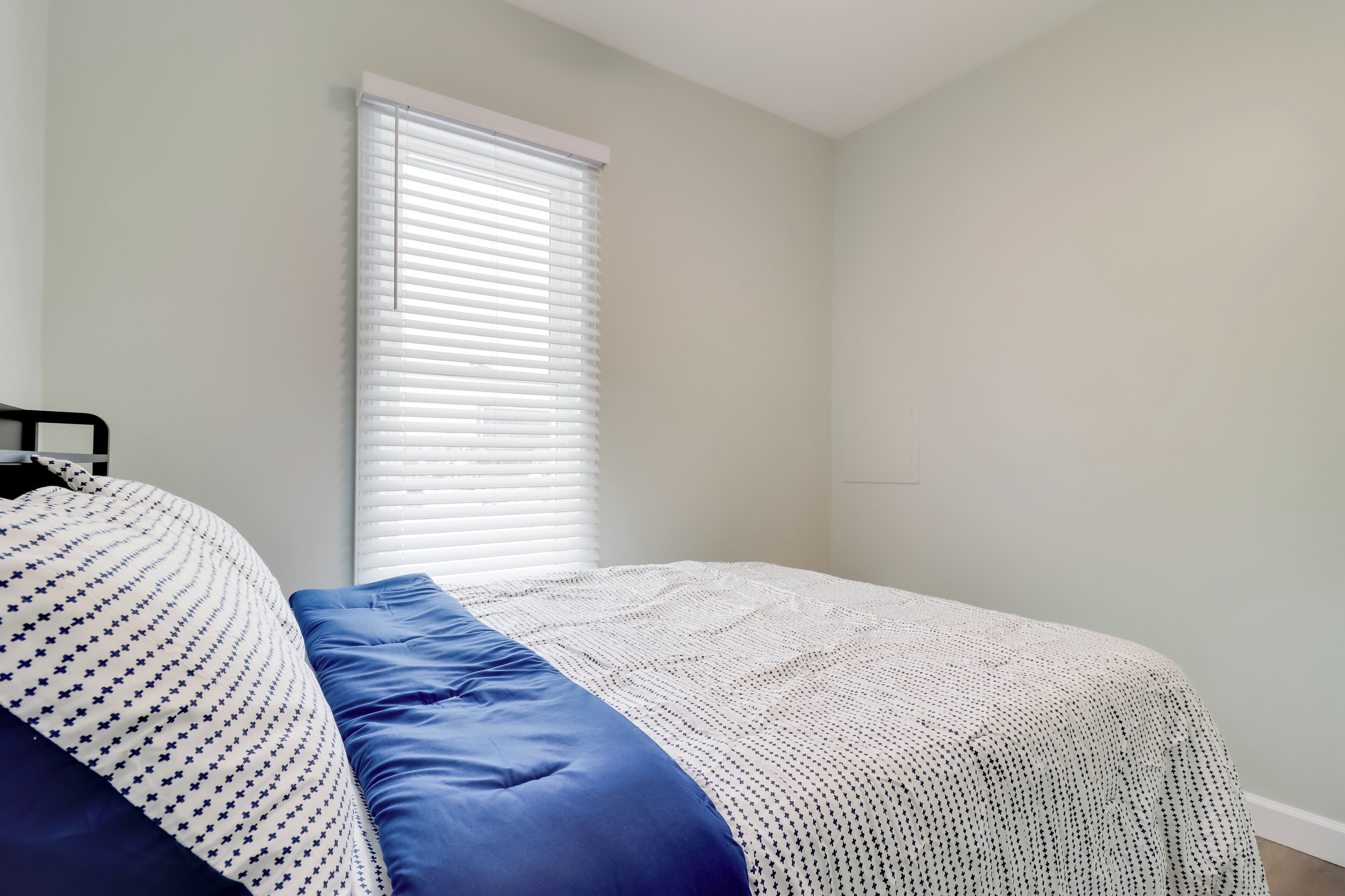 Quarto com cama, janela com persianas e parede lisa.