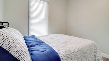 Quarto com cama, janela com persianas e parede lisa.