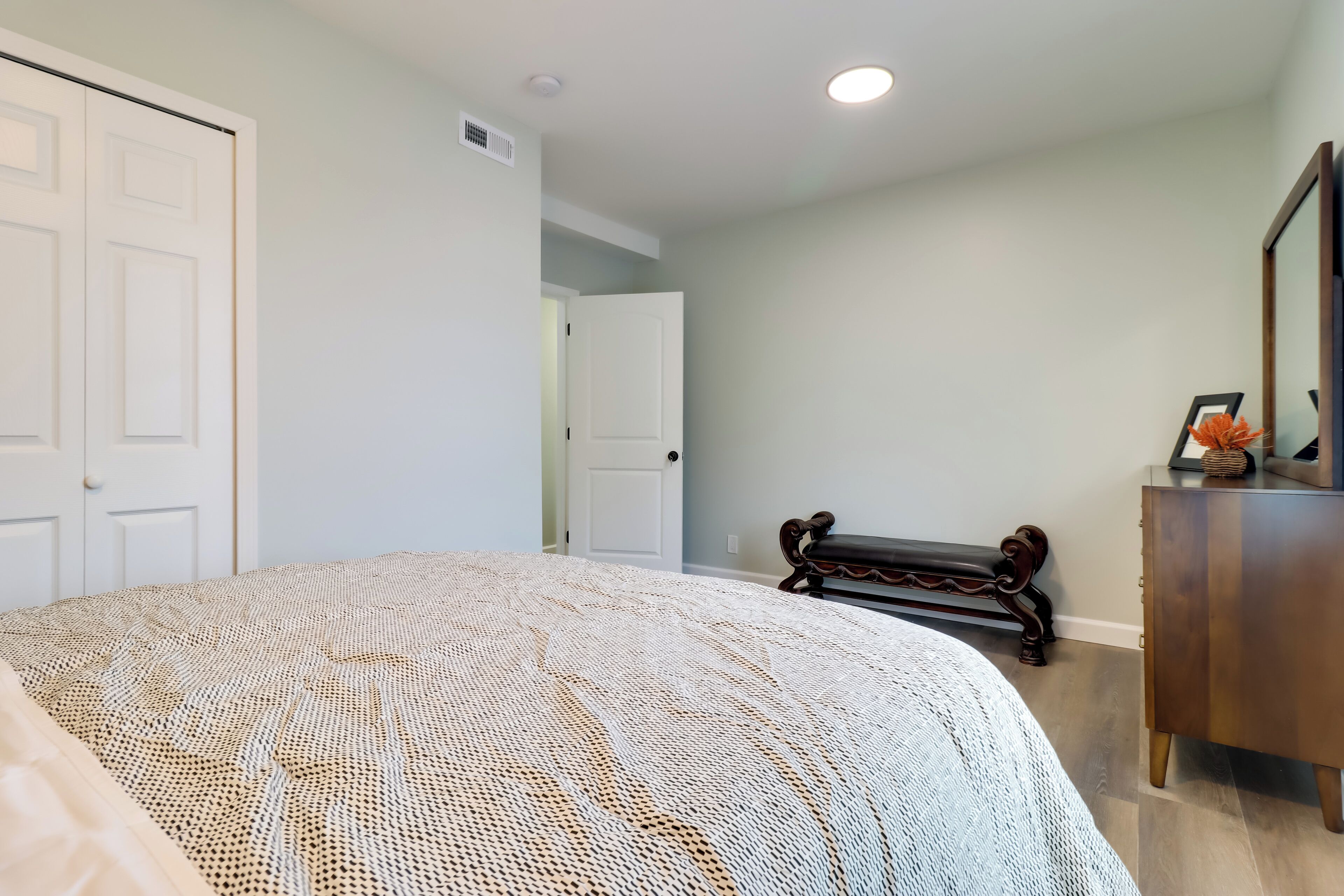 Un dormitorio con una cama grande, un banco de madera, un aparador y una puerta que da a otra habitación.