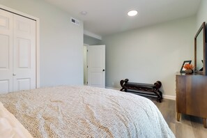 Ein Schlafzimmer mit einem großen Bett, einer hölzernen Bank, einem Schminktisch und einer Tür zu einem anderen Raum.