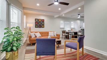 Uma sala de estar moderna com um sofá, cadeiras, uma mesa de jantar e uma cozinha ao fundo.