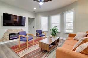 Ein modernes Wohnzimmer mit Kamin, zwei violetten Sesseln, einem Holztisch und einem orangefarbenen Sofa.
