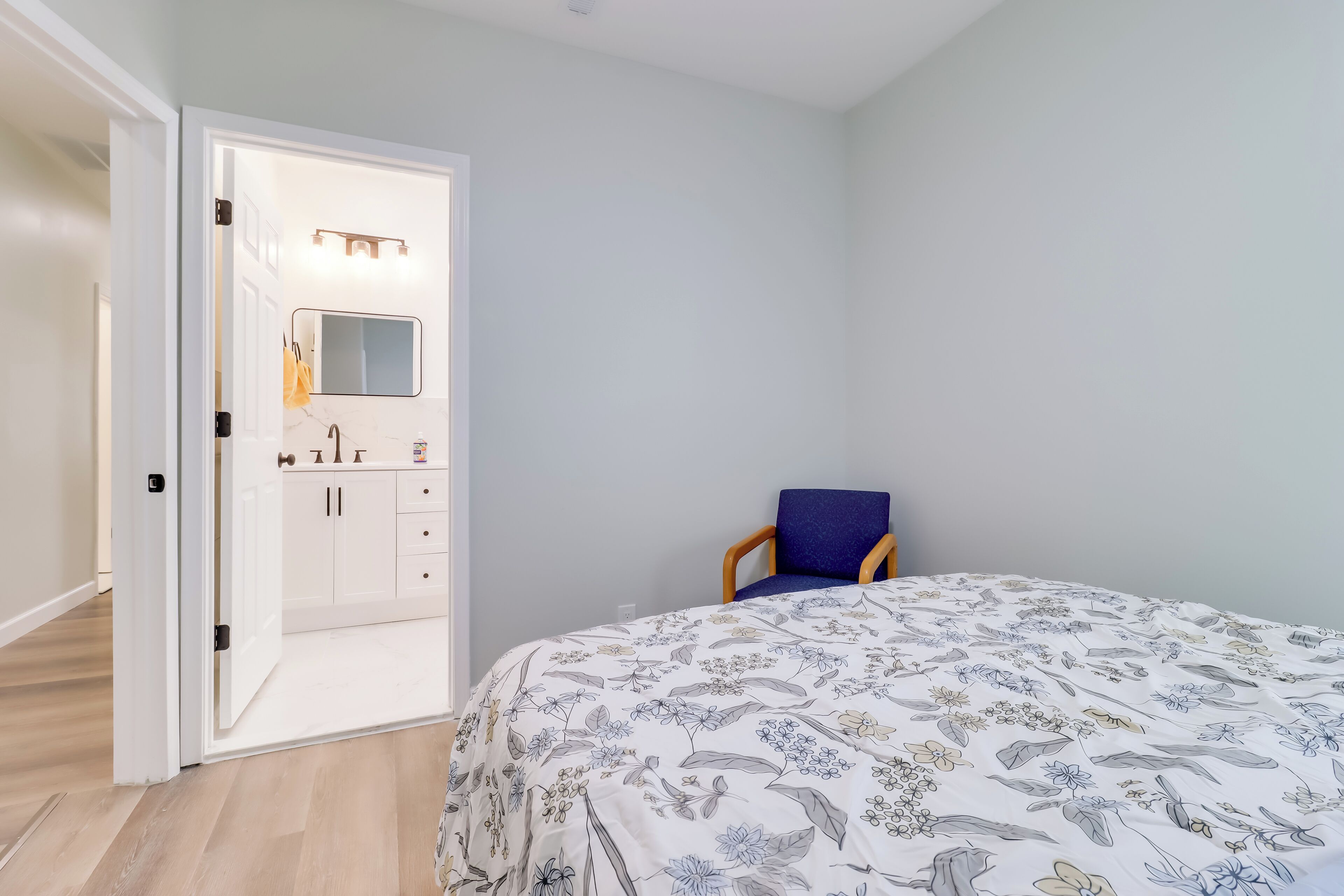 Une chambre à coucher avec un lit, une chaise, une armoire et une salle de bain visible à travers une porte ouverte.