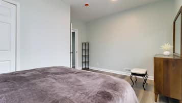 Un dormitorio con una cama grande, un aparador de madera, un taburete pequeño y una puerta que da a otra habitación.