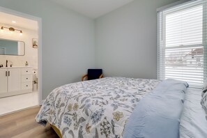 Ein Schlafzimmer mit einem Bett, einem Sessel, einem Frisiertisch mit Spiegel und einem Fenster mit Jalousien.