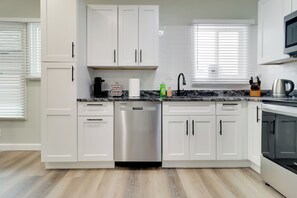 Cozinha moderna com armários brancos, lava-louças de aço inoxidável e bancada preta.