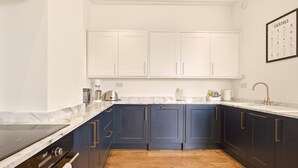 A kitchen with dark blue cabinets, a white countertop, a stainless steel range hood, and a wooden floor. - Sunset Views - North East Escapes (Tynemouth)