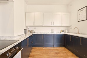 A kitchen with dark blue cabinets, a white countertop, a stainless steel range hood, and a wooden floor. - Sunset Views - North East Escapes (Tynemouth)