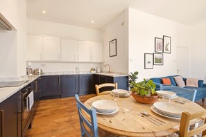 Une cuisine moderne avec des meubles blancs, une table à manger pour quatre personnes et un canapé bleu dans l’espace salon.