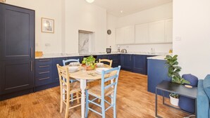 A modern kitchen with dark blue cabinets, a round wooden table, and blue chairs. - Sunset Views - North East Escapes (Tynemouth)