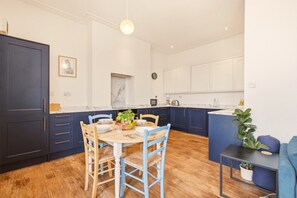 A modern kitchen with dark blue cabinets, a round wooden table, and blue chairs. - Sunset Views - North East Escapes (Tynemouth)
