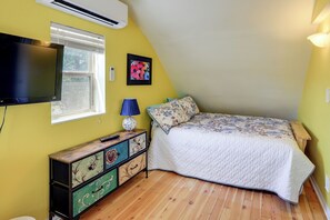Quarto com cama, televisão, janela, ar condicionado fixado na parede e mesa de cabeceira com abajur.