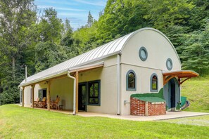 A single-story building with a curved roof, a covered porch with seating, and a brick extension. - Outdoor Kitchen! 'the Hobbit House' on Elk River (Elk Park)