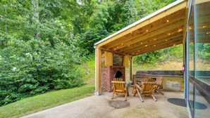 Una veranda esterna con camino in mattoni, sedie di legno e barbecue.