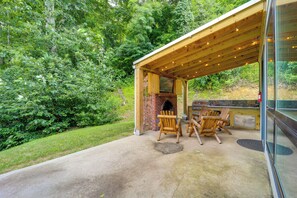 Eine Terrasse im Freien mit Kamin aus Ziegelsteinen, Holzstühlen und einem Grill.
