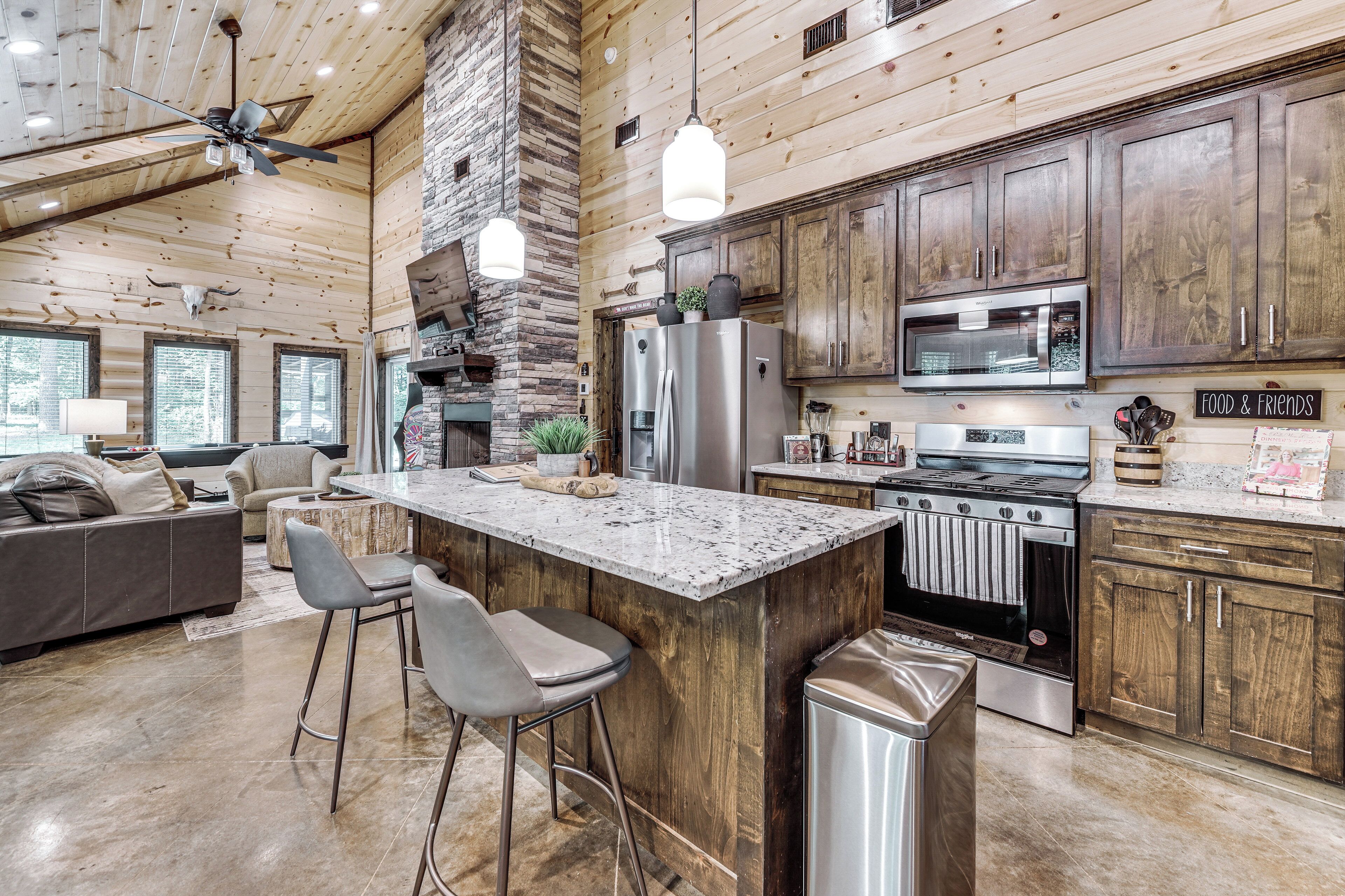 Una cocina amplia con una isla central, taburetes de bar, chimenea de piedra y electrodomésticos modernos.