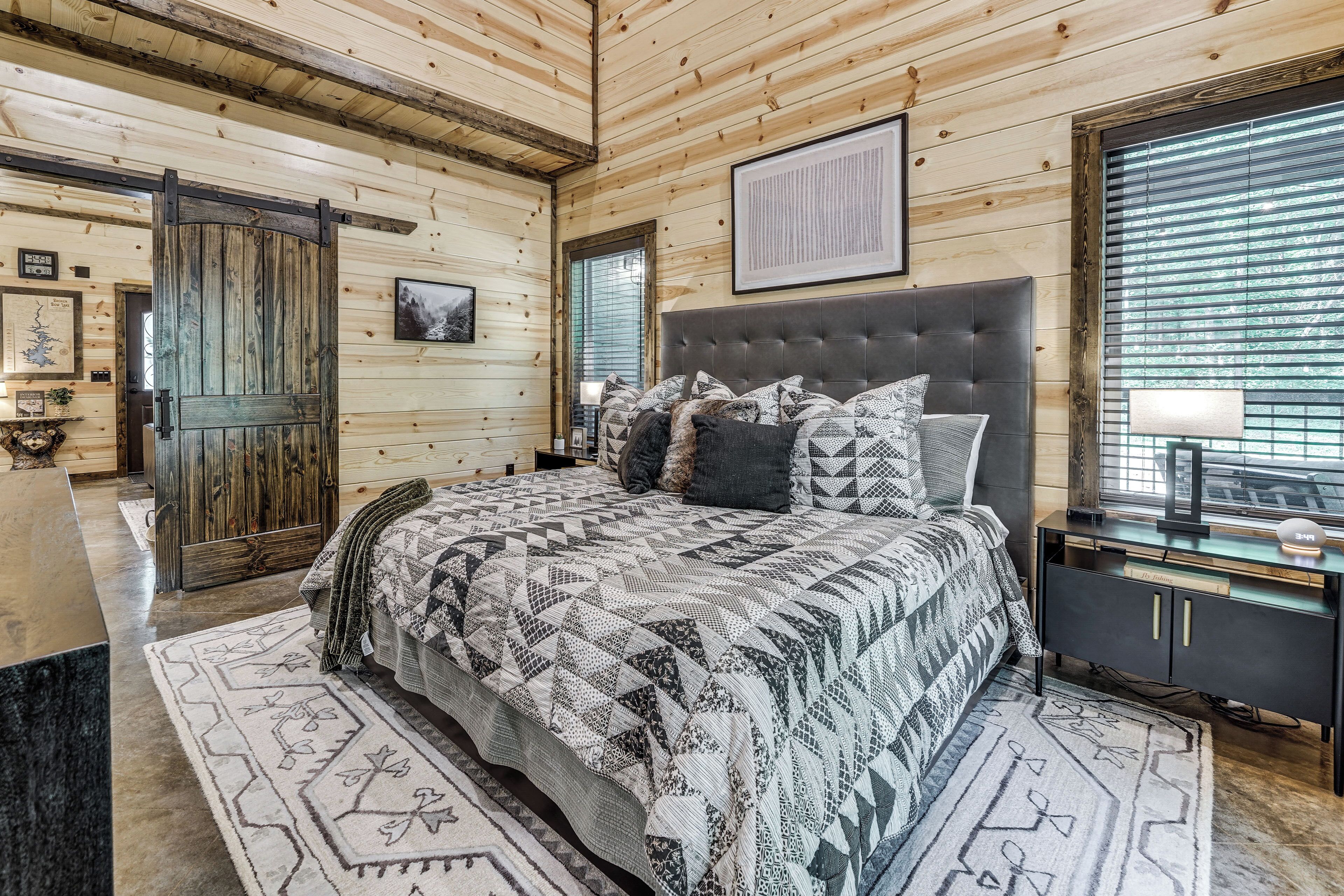 A bedroom with a large bed, a wooden door, a framed picture, and a window with blinds.