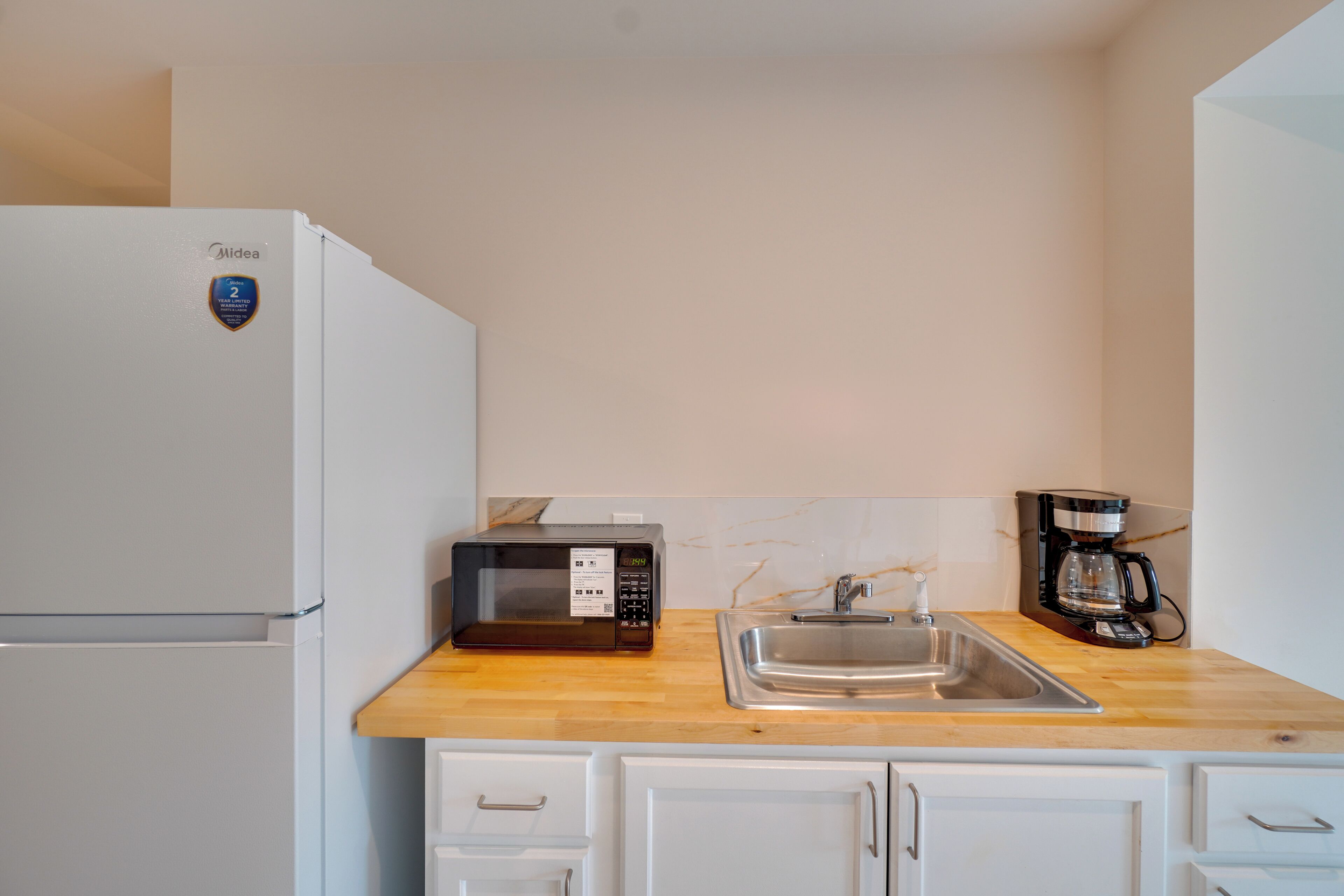 Cocina compacta con refrigerador blanco, microondas, cafetera y pileta de acero inoxidable.