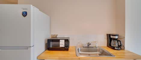 Cocina compacta con refrigerador blanco, microondas, cafetera y pileta de acero inoxidable.