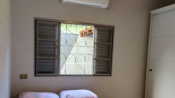 Un dormitorio con cama, ventilador de techo, aire acondicionado y ventana con rejas.