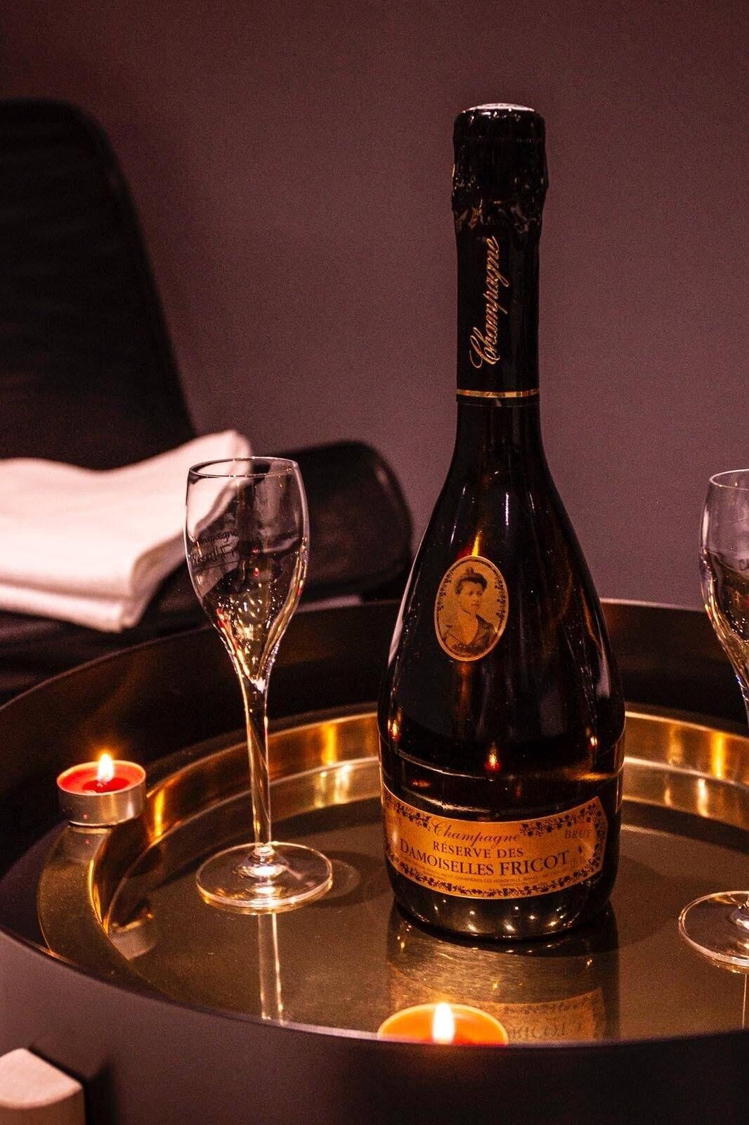 A bottle of champagne on a tray with two glasses and candles.
