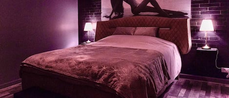 A bedroom with a large bed, two bedside lamps, a bench, and a wall mural.