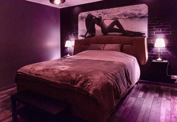 A bedroom with a large bed, two bedside lamps, a bench, and a wall mural.