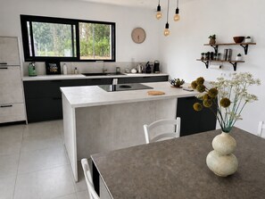 A modern kitchen with a large island, built-in appliances, and a dining area with a vase of flowers. - L'Aure Mar; Sunny villa 5 minutes from the beach (Saint-Cyprien)