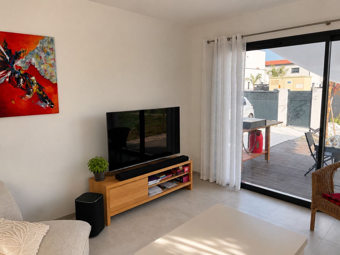 Una sala moderna con un televisor de pantalla plana sobre un soporte de madera, un sofá, una mesa de centro y un puerta corrediza de vidrio que da a un espacio exterior.