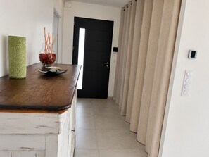 A hallway with a wooden table, a green vase, and a bowl of flowers. A black door and beige curtains are visible. - L'Aure Mar; Sunny villa 5 minutes from the beach (Saint-Cyprien)