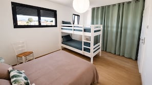 A bedroom with bunk beds, a chair, a bed with a floral pillow, a window with blinds, and a curtain. - L'Aure Mar; Sunny villa 5 minutes from the beach (Saint-Cyprien)