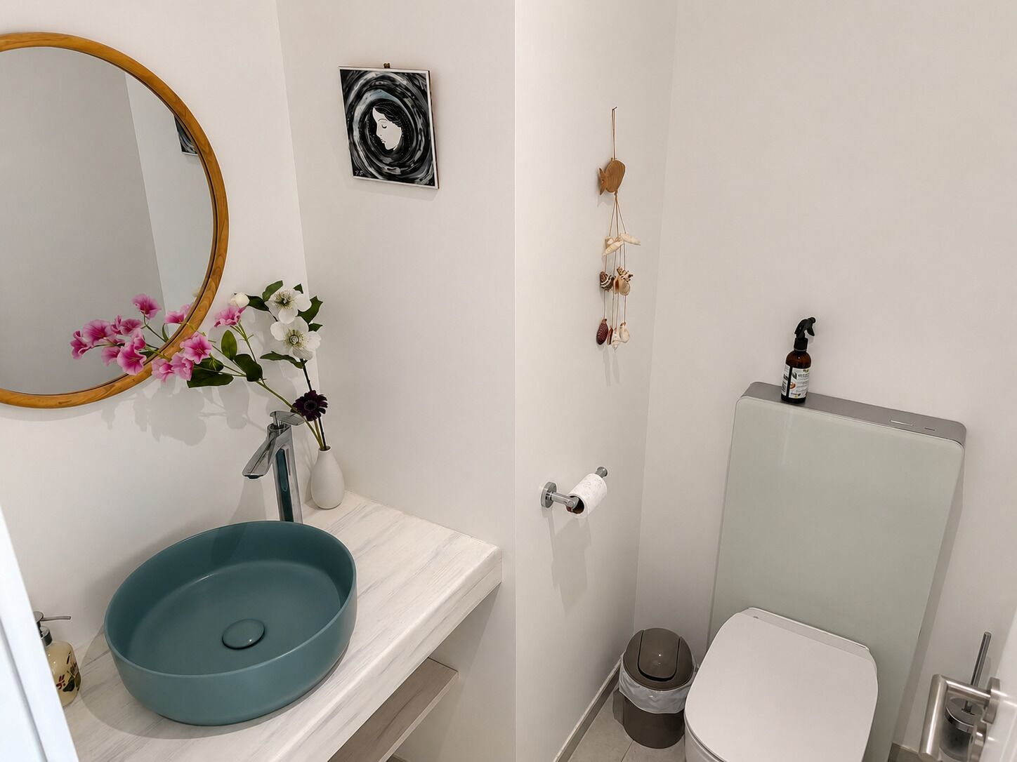 A bathroom with a round mirror, a blue sink, a toilet, and a wall-mounted toilet paper holder.