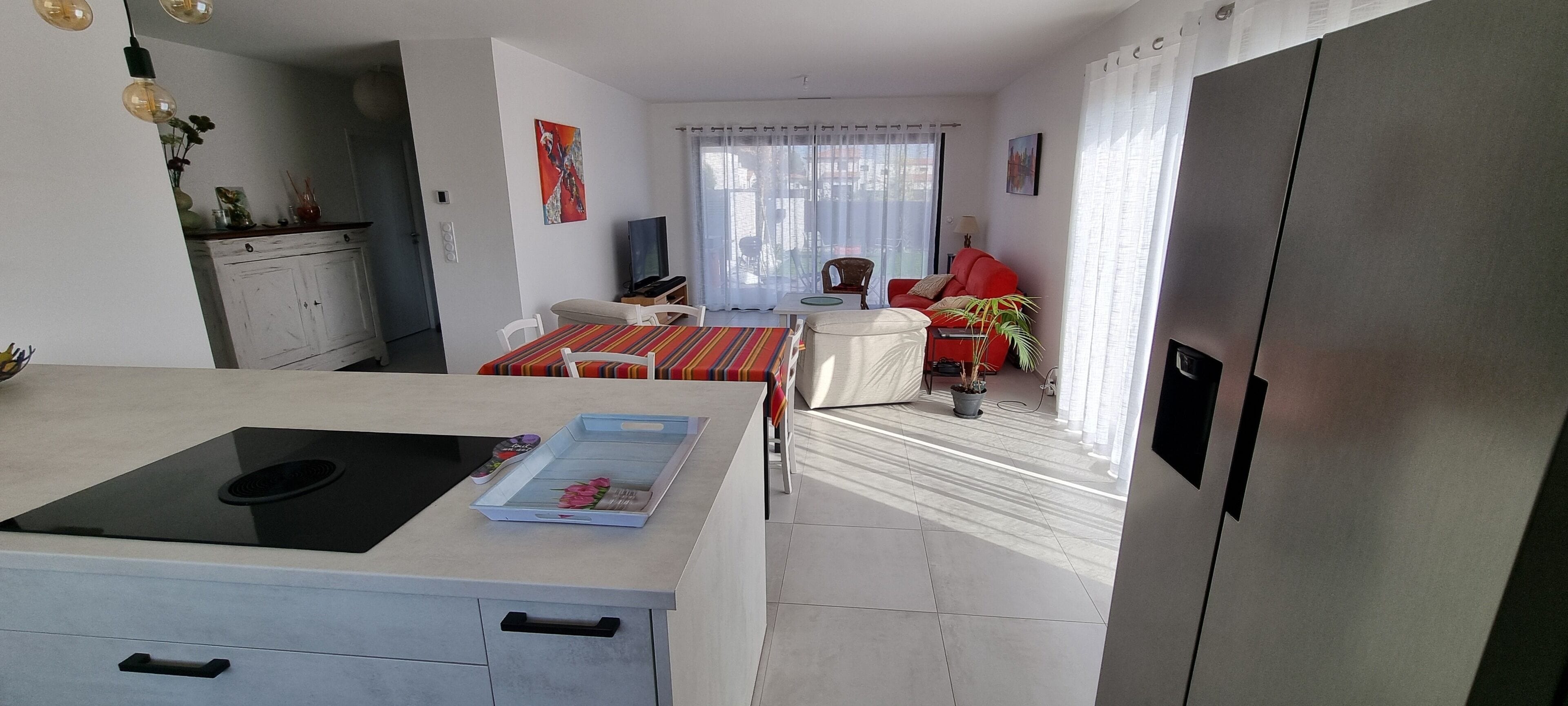 A modern kitchen with a built-in stove, a dining area with a striped tablecloth, and a red sofa.