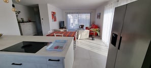 A modern kitchen with a built-in stove, a dining area with a striped tablecloth, and a red sofa. - L'Aure Mar; Sunny villa 5 minutes from the beach (Saint-Cyprien)